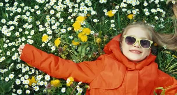 Fille couchée dans l'herbe et regardant la caméra. Fille en manteau rouge et lunettes de soleil. Panoramique — Video