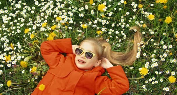Zbliżenie portret dziecko, leżąc na trawie i patrząc na kamery. Kciuk w górę. Ok. Dziewczyna śpiewa piosenkę — Wideo stockowe