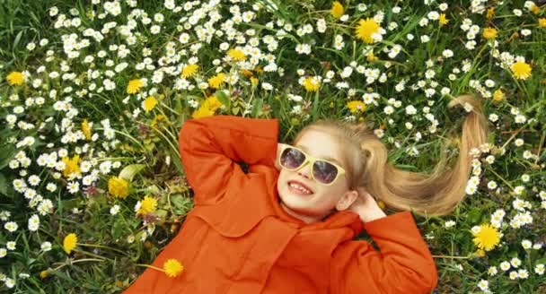 Zbliżenie portret dziecko, leżąc na trawie i patrząc na kamery. Kciuk w górę. Ok. Dziewczyna śpiewa piosenkę. Płukanie — Wideo stockowe