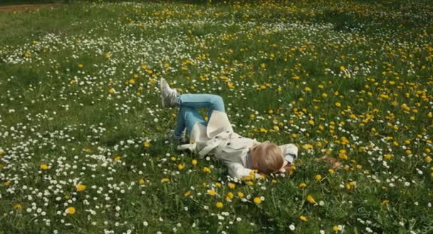 Погода весна. Ребенок лежит на траве и ничего не делает. Девушка смотрит на небо и камеру — стоковое видео