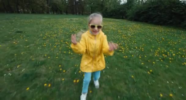 Criança a correr numa clareira de dentes-de-leão. Afasta-se da câmara. Olhando para a câmera — Vídeo de Stock