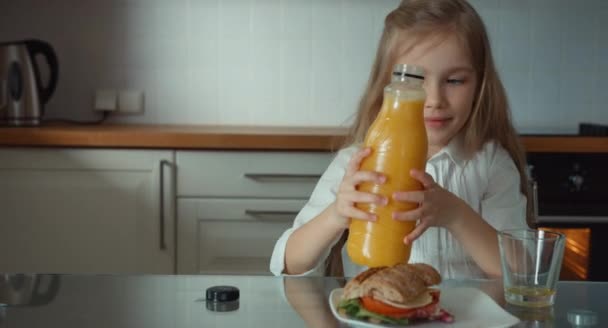 Παιδί που χύνεται πορτοκαλί χυμό σε ένα ποτήρι και πιείτε το στην κουζίνα — Αρχείο Βίντεο
