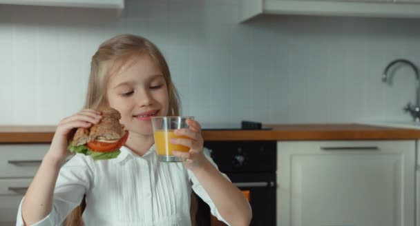 Menina criança satisfeita segurando um sanduíche e um copo de suco de laranja — Vídeo de Stock