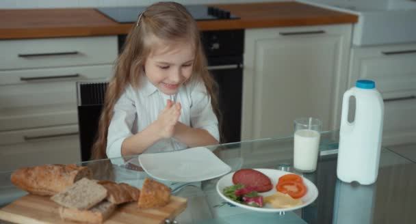 Levez le pouce. D'accord. Portrait d'une fille dans la cuisine. Près de l'enfant est une miche de pain, laitue, fromage, saucisse et un verre de lait. La fille préparera un sandwich. Elle boit du lait — Video