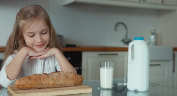 Πορτρέτο του ένα preschooler κορίτσι στην κουζίνα. Κοντά στο παιδί είναι ένα καρβέλι ψωμί και ένα ποτήρι γάλα — Αρχείο Βίντεο