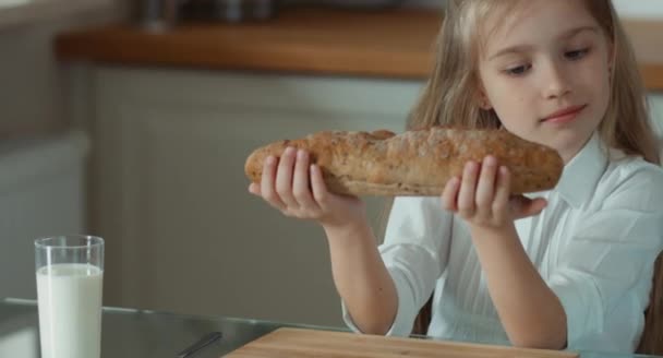 Barnet håller en limpa bröd. Flickan tittar på kameran och leende — Stockvideo