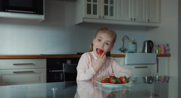 Criança comendo um grande morango vermelho e olhando para a câmera. Está bem. — Vídeo de Stock