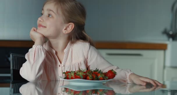 Belle petite fille et une grande assiette de fraises. Enfant regardant la caméra et souriant — Video