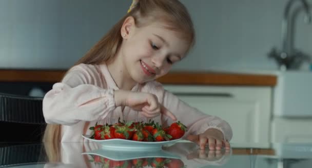 Mädchen lacht und blickt in die Kamera. Neben ihr steht ein großer Teller mit Erdbeeren — Stockvideo