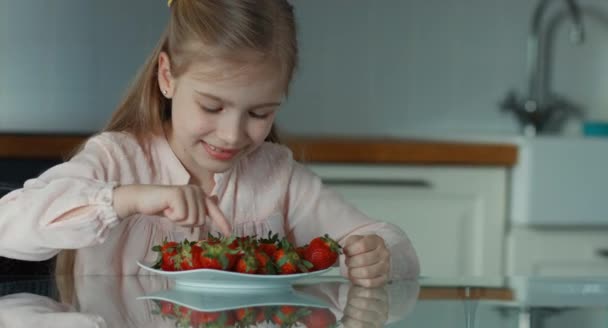 Retrato de perto criança rindo e olhando para a câmera. Polegares para cima. Ao lado dela está um prato grande de morangos. — Vídeo de Stock