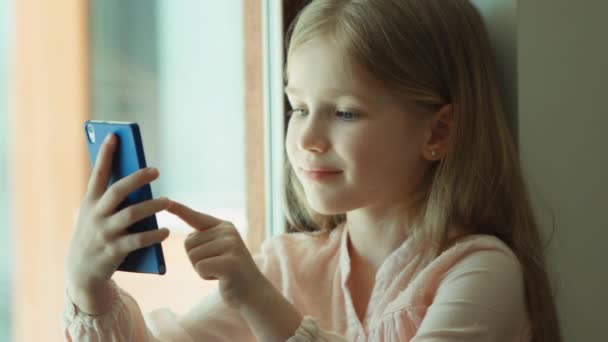Closeup portret kind. Meisje met behulp van de mobiele telefoon en glimlachen. Camera kijken. Ziet u ok. Duimschroef opwaarts — Stockvideo