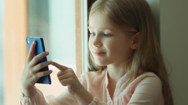 Primer plano retrato niño. Chica usando el teléfono móvil y sonriendo. Mirando la cámara. Muestra bien. Pulgares arriba — Vídeo de stock