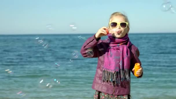 Meisje bubbels op het strand van zee waait. Kind kijken camera — Stockvideo