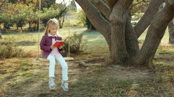 Доїльна дівчина обіймає книжки і дивиться на камеру. Дитина сидить на гойдалці — стокове відео