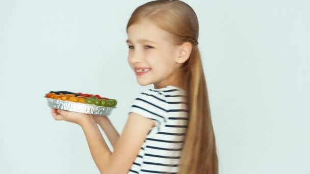 Closeup πορτρέτο κορίτσι εκμετάλλευση κέικ με φρούτα κοντά πρόσωπο το λευκό φόντο — Αρχείο Βίντεο
