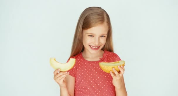 Menina segurando pedaço de melão amarelo no fundo branco. Criança mostrando melão na câmera — Vídeo de Stock