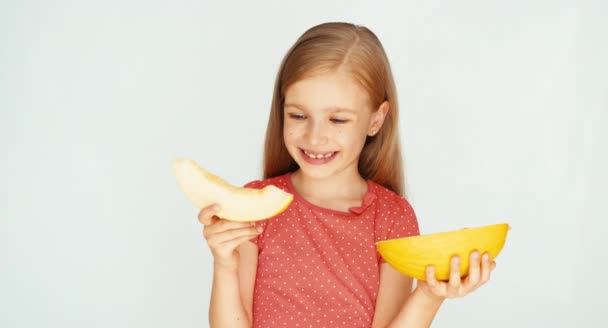 Девушка ест желтую дыню на белом фоне. Очень вкусная дыня. Ребёнок показывает дыню на камеру — стоковое видео