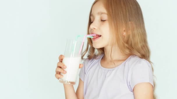 Niño sonriente bebiendo leche. Chica con hermoso cabello rubio sobre un fondo blanco. Pulgar hacia arriba. De acuerdo, de cerca. — Vídeos de Stock