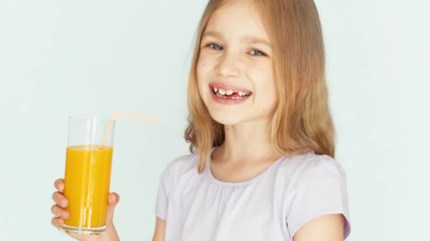 Chica sosteniendo un vaso de jugo de naranja y riéndose de la cámara. Chica con hermoso cabello rubio sobre un fondo blanco. Pulgar hacia arriba. De acuerdo, de cerca. — Vídeos de Stock