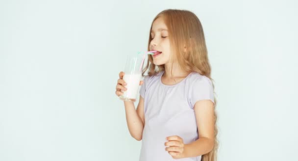 Niño sonriente bebiendo leche. Chica con hermoso cabello rubio sobre un fondo blanco. Pulgar hacia arriba. Ok. — Vídeo de stock