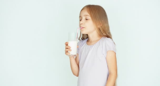 Lyckligt barn dricka mjölk. Tjej med vackra blonda hår på en vit bakgrund. Tummen upp. Okej — Stockvideo
