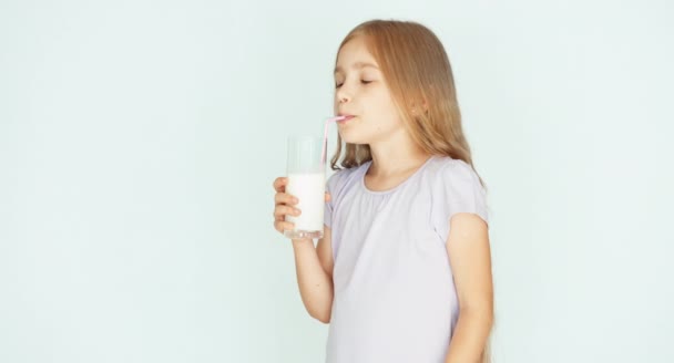 Bambino felice che beve latte. Ragazza con bei capelli biondi su uno sfondo bianco. Pollice in alto. Va bene. — Video Stock