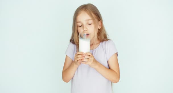 Kind schnüffelt Milch. Mädchen zeigt Glas Milch vor der Kamera. Mädchen mit schönen blonden Haaren auf weißem Hintergrund. Daumen hoch. ok — Stockvideo