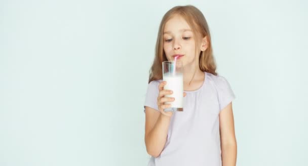 Niño bebiendo leche de vidrio. Chica con hermoso cabello rubio sobre un fondo blanco — Vídeos de Stock