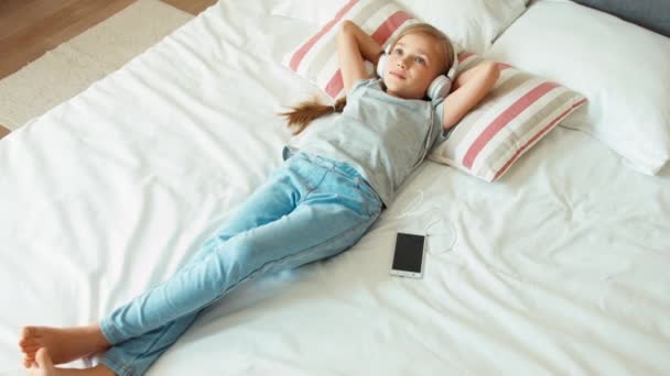 Flicka barn lyssnar musik hörlurar och ligger på sängen. Zoomning — Stockvideo