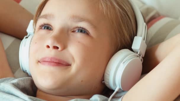 Extremo primer plano retrato chica escuchar música en los auriculares con los ojos cerrados y acostado en la cama — Vídeo de stock