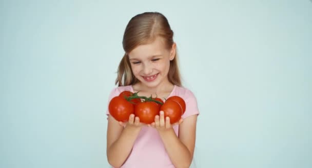 Flickan håller tomater och ler mot kameran på den vita bakgrunden — Stockvideo