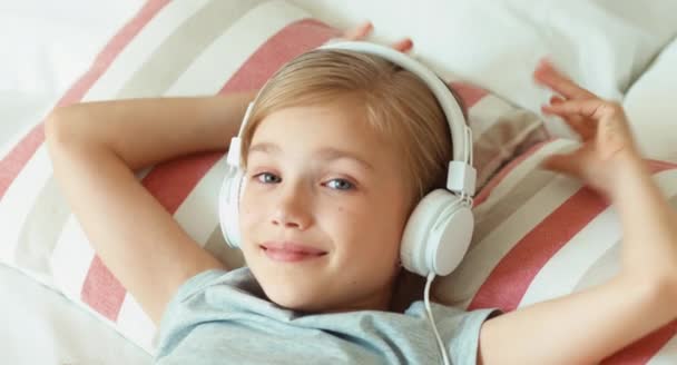 Closeup portrait girl child listening music in headphones and resting lying on the be — Stock Video