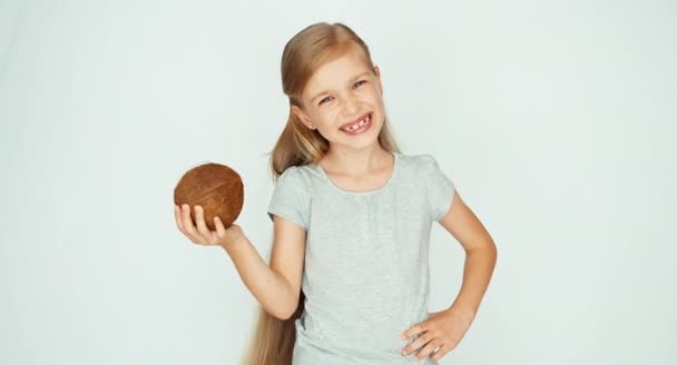 Девушка играет, показывает кокос и смеется над камерой. Ребенок с фруктами на белом фоне — стоковое видео