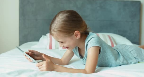 Mädchen mit Tablet-PC spielen. Kind liegt auf dem Bett — Stockvideo