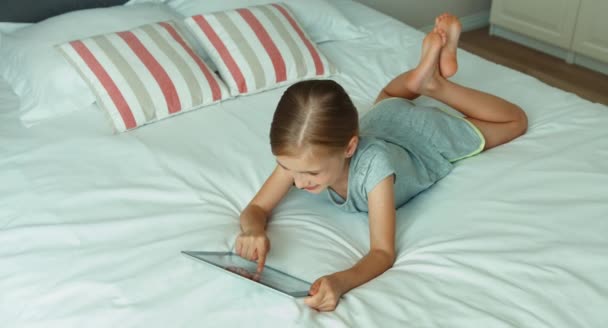 Girl using tablet pc. Child lying on the bed and laughing at camera. Top view — Stock Video