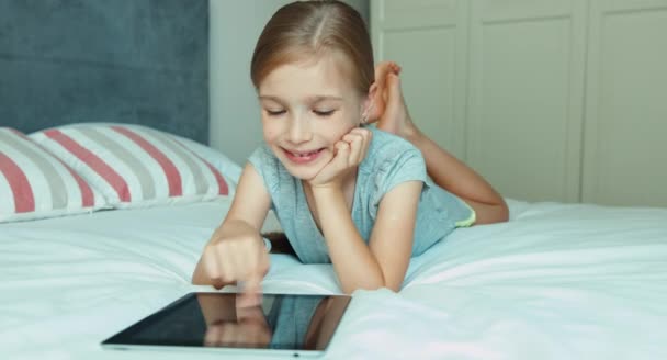 Mädchen mit Tablet-PC auf dem Bett liegend und lachend in die Kamera. Große Augen überraschen — Stockvideo