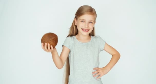 Девушка играет, показывает кокос и смеется над камерой. Ребёнок с фруктами на белом фоне. Пальцем вверх. Хорошо. — стоковое видео