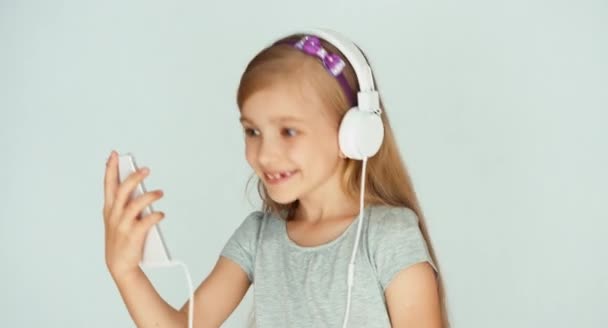 Chica escuchando música con un smartphone y bailando sobre un fondo blanco — Vídeos de Stock