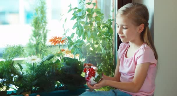 Girl eating ice cream and smiling at the camera. Child sitting on the windowsill — Stock video