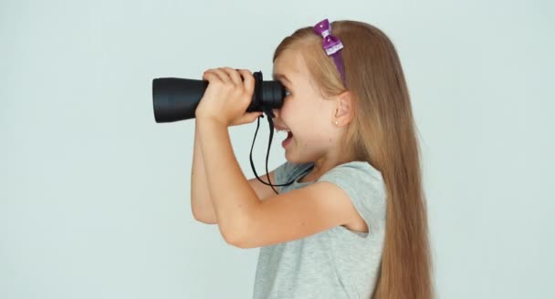 Ragazza che guarda attraverso il binocolo davanti alla telecamera. Ragazza che ride su uno sfondo bianco. Pollice in alto. Va bene. — Video Stock