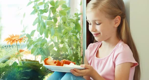 Portrait girl sniffing tomato against window and offers at camera — Αρχείο Βίντεο