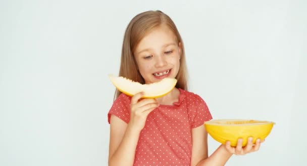 Girl eating yellow melon on the white background. Child showing melon at camera — ストック動画