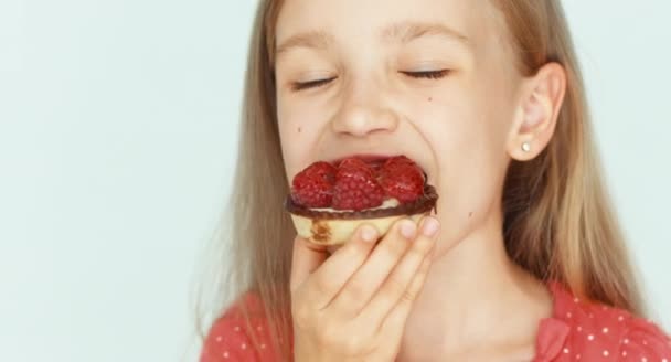 Chica comiendo un pastel con frambuesas. Chica con hermoso cabello rubio sobre un fondo blanco. Primer plano. — Vídeos de Stock