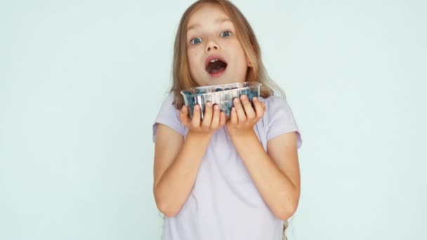 Mädchen schnüffelt an Blaubeeren und zeigt in die Kamera auf dem weißen Hintergrund. glückliches Kind mit Früchten. Zoomen — Stockvideo