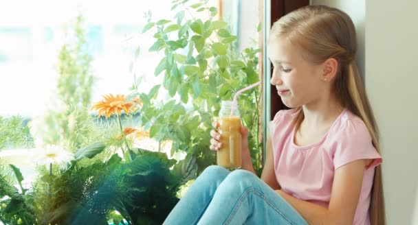 Chica bebiendo jugo y sentado en el alféizar de la ventana y sonriendo a la cámara — Vídeos de Stock