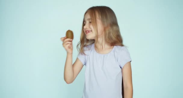 Girl sniffing kiwi and showing at camera on the white background. Thumb up. Ok — ストック動画