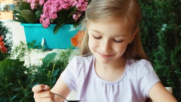 Mädchen, das sehr leckere Blaubeeren mit Zucker isst und nickt. Kind sitzt auf dem Tisch im Garten — Stockvideo