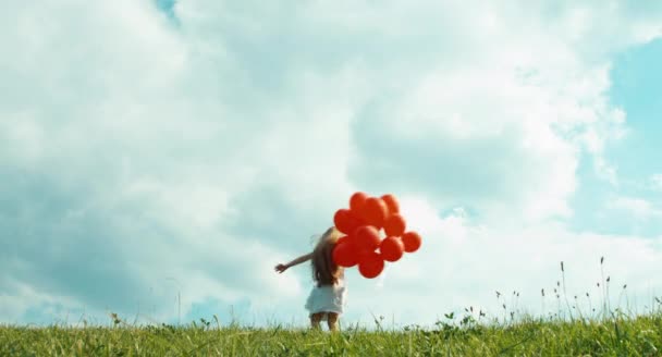 Chica en un vestido blanco sosteniendo globos rojos y girando contra el cielo en tiempo nublado — Vídeos de Stock