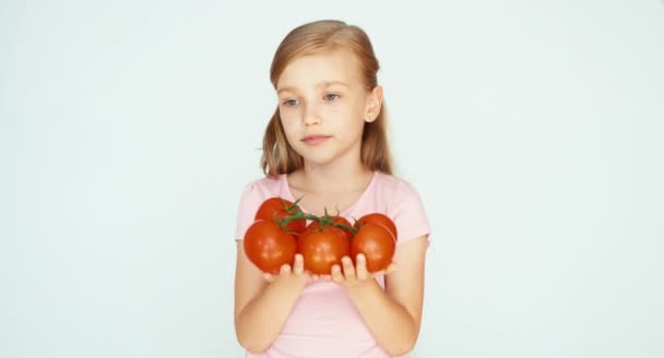 Chica oliendo tomates y sosteniendo vegetales en las manos y sonriendo a la cámara en el fondo blanco — Vídeo de stock