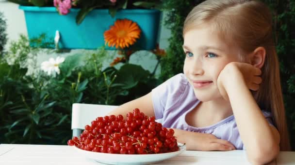 Girl has a big plate of red currant. Child sitting resting on the table in the garden. Zooming — Αρχείο Βίντεο